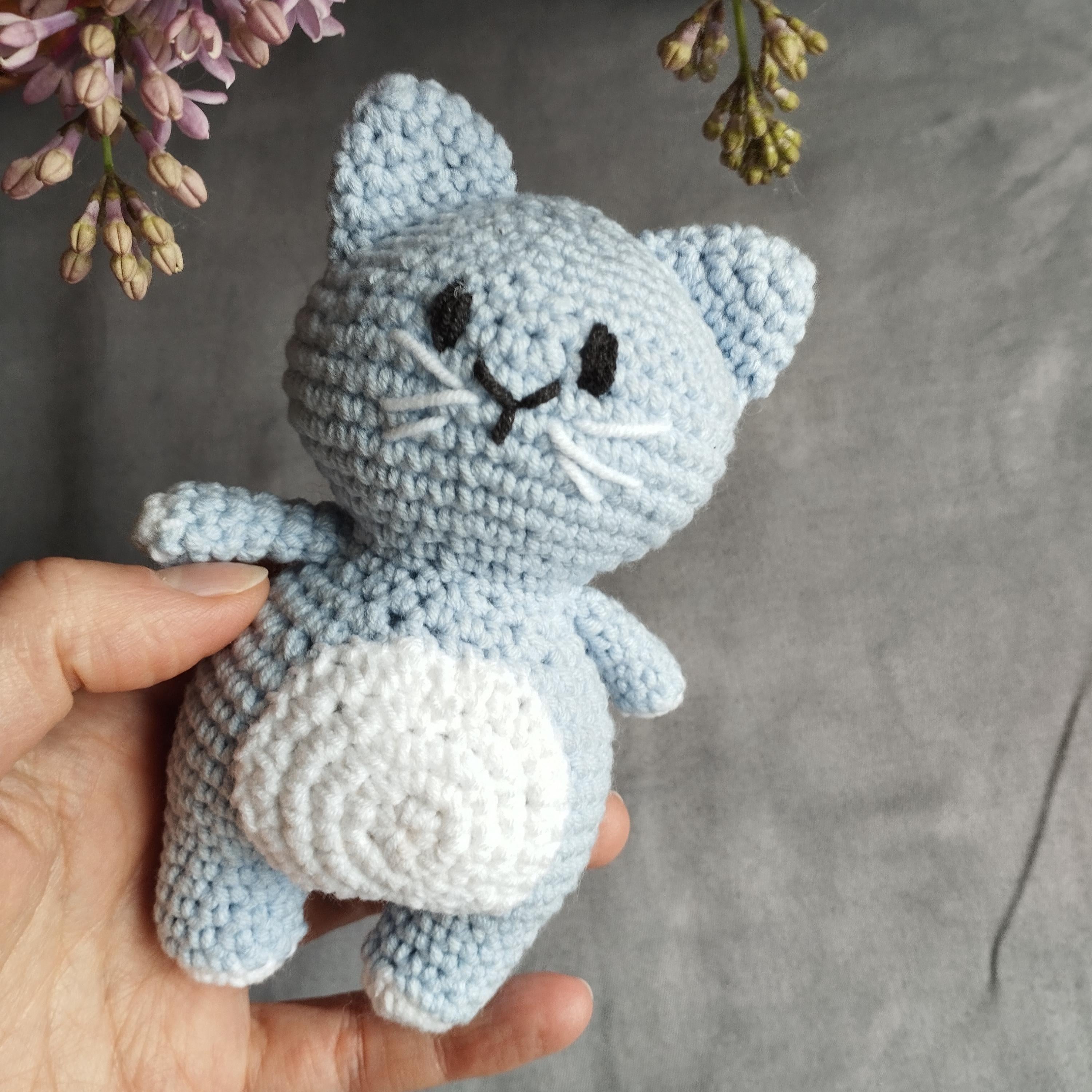 a hand holding a small blue crocheted cat
